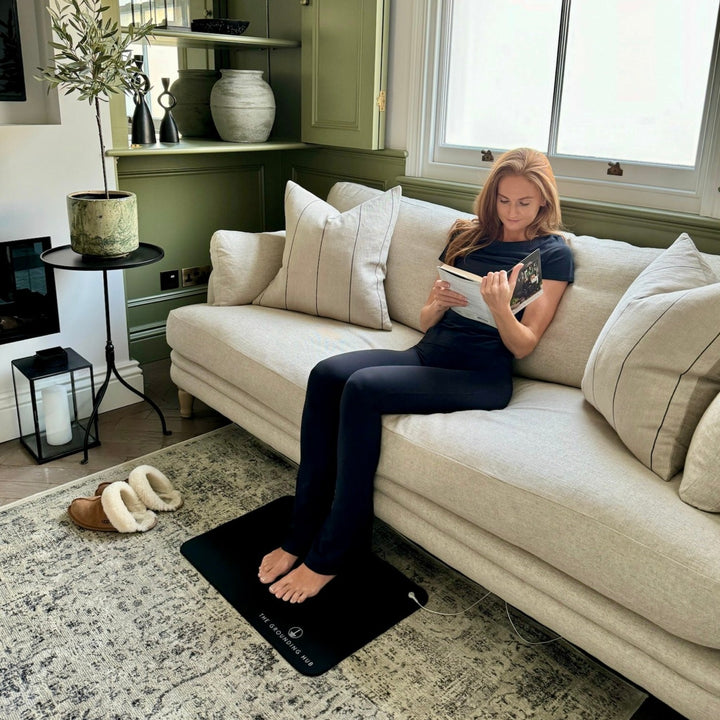 A lady relaxing with a book on a sofa with feet resting on her grounding mat